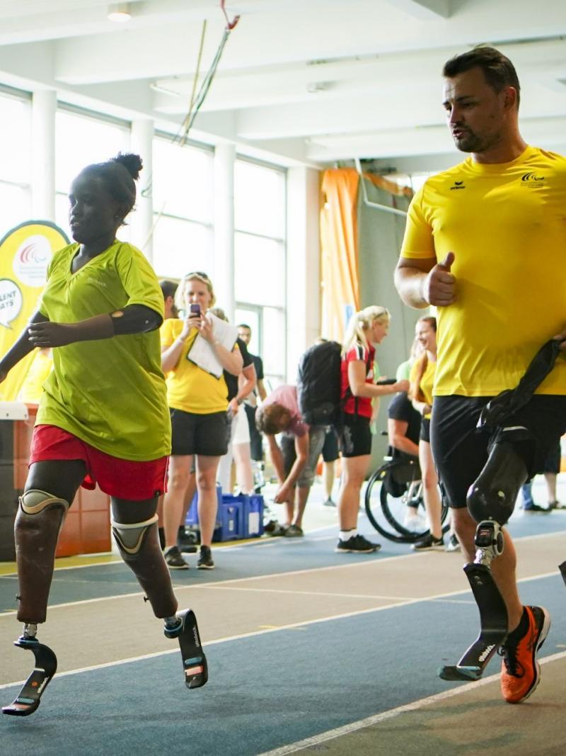 Male sprinter with prothesis runs alongside a young double-amputee sprinter girl