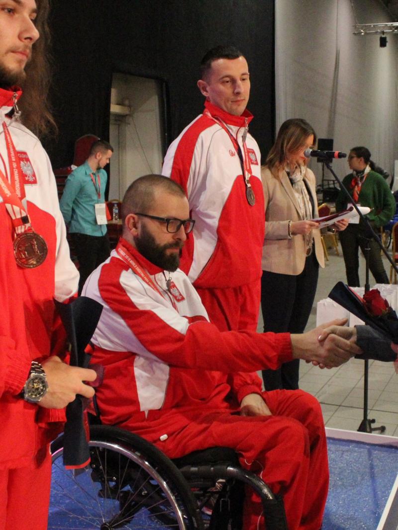 Man in wheelchair shakes hand with woman during medal ceremony