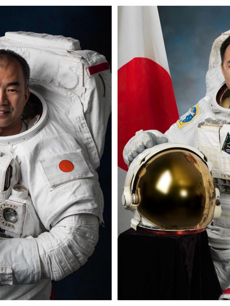 two male astronauts smiling in their space suits and standing beside the Japan flag