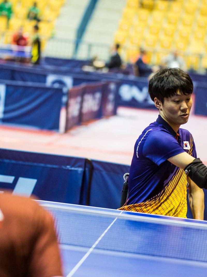 Male Korean table tennis playe in wheelchair hits a backhand shot