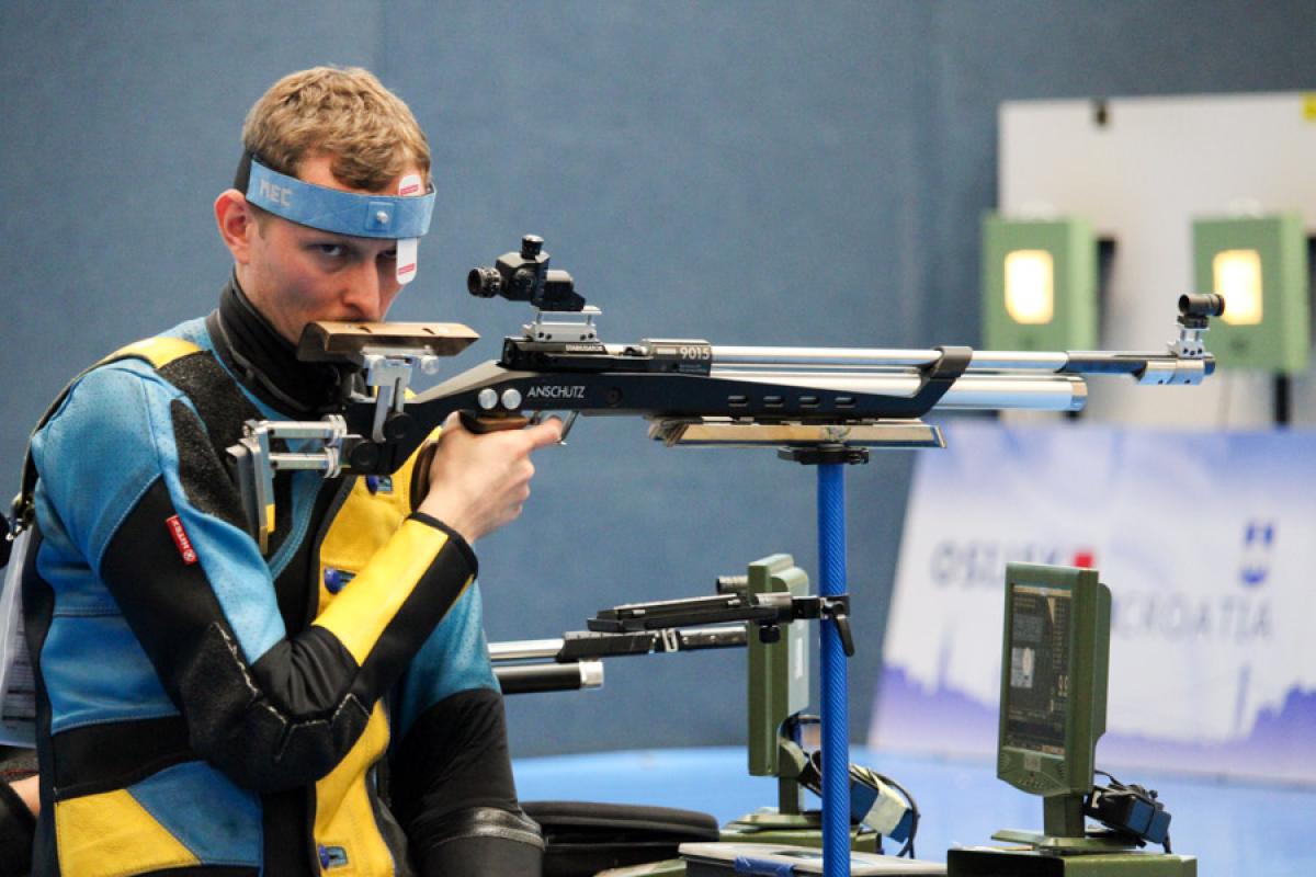 A man with a rifle in a sitting position at a shooting range