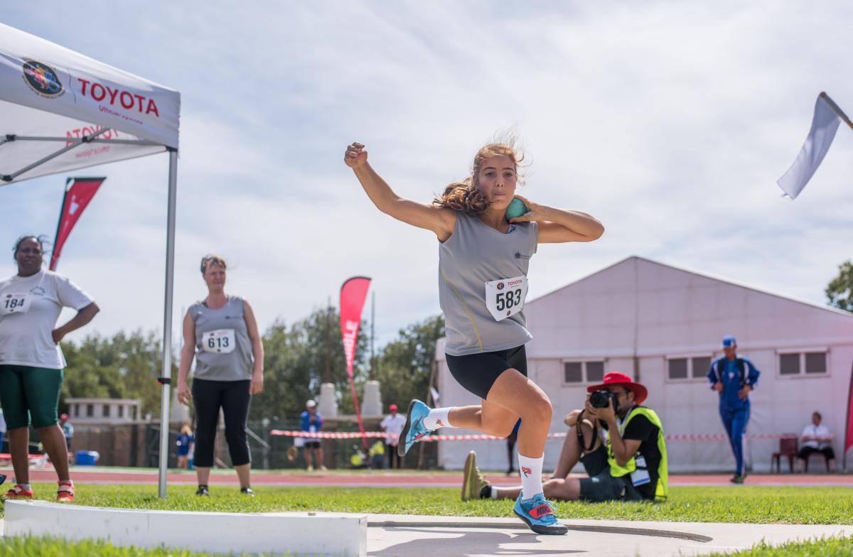 A female teenage athlete competing in shot put watched by three people