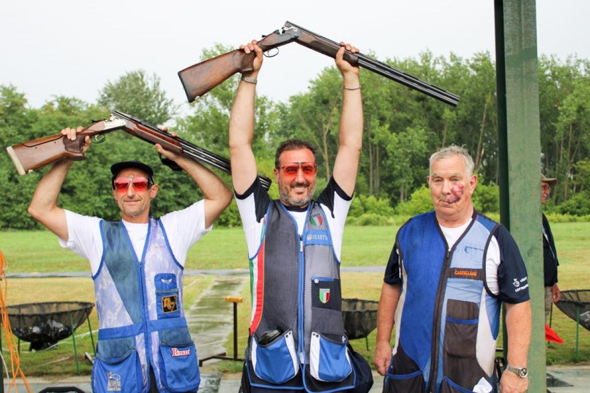 Three male Para trap shooters pose together with man in middle raising his shot gun over his head