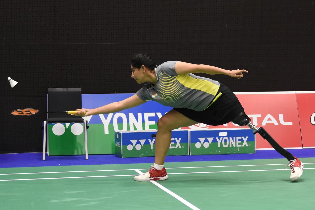 a female Para badminton player with a prosthetic leg reaches for a shot