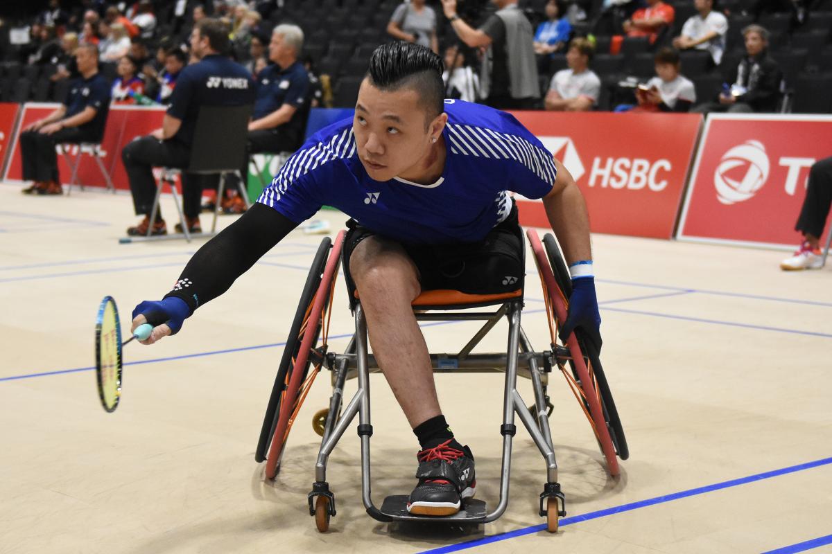 Hong Kong badminton player in wheelchair leans over to return a shot