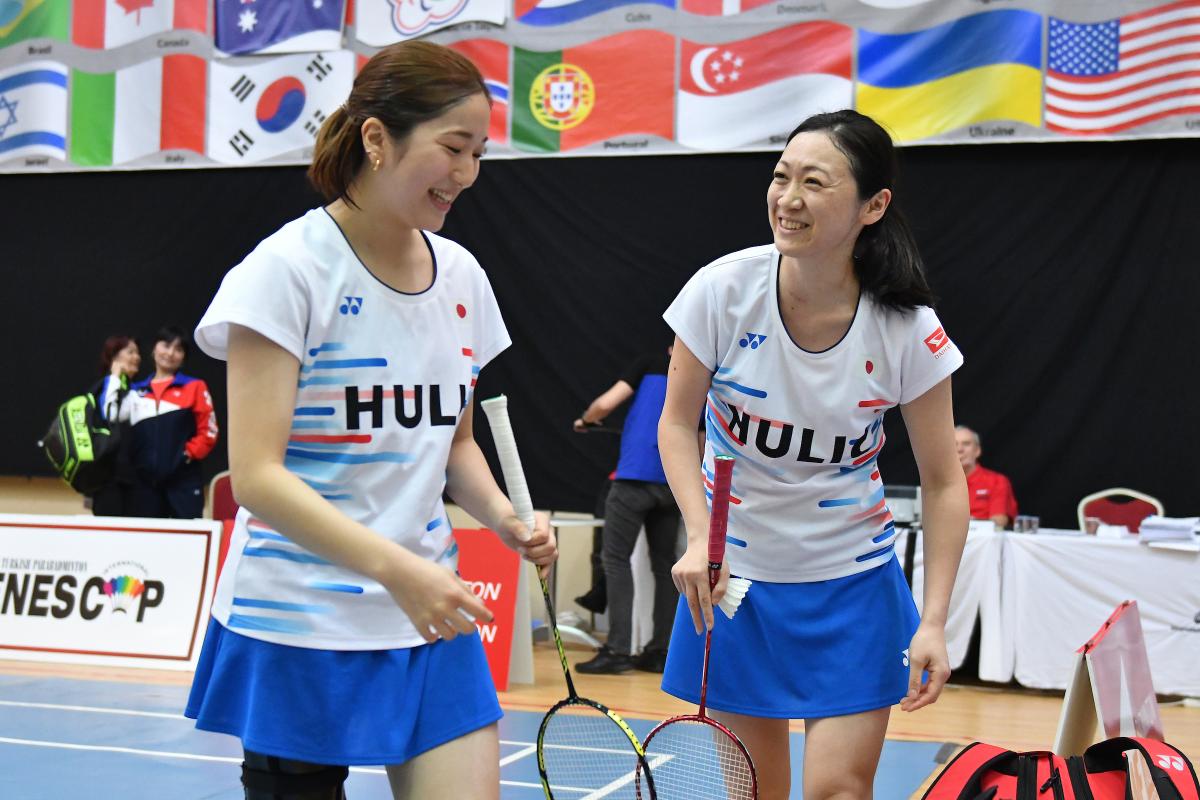 two female standing Para badminton players laughing together on court