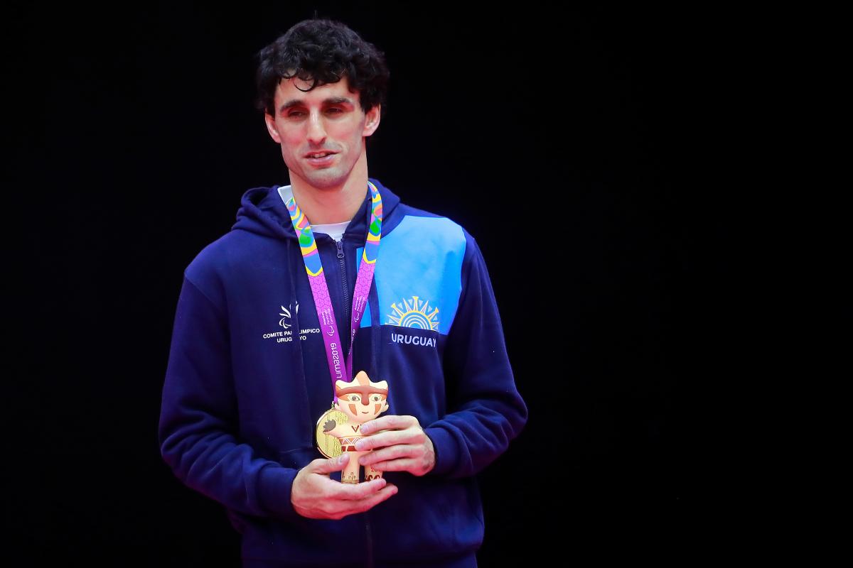 a male judoka stands on the podium with his gold medal