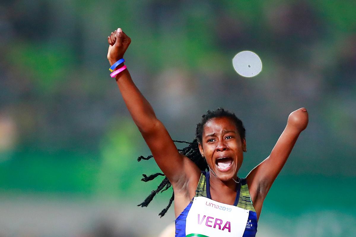 a female Para athlete raises her arms in celebration on the finish line