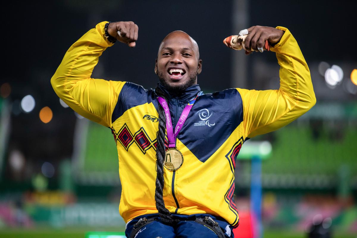 a male wheelchair athlete with a gold medal round his neck raises his arms