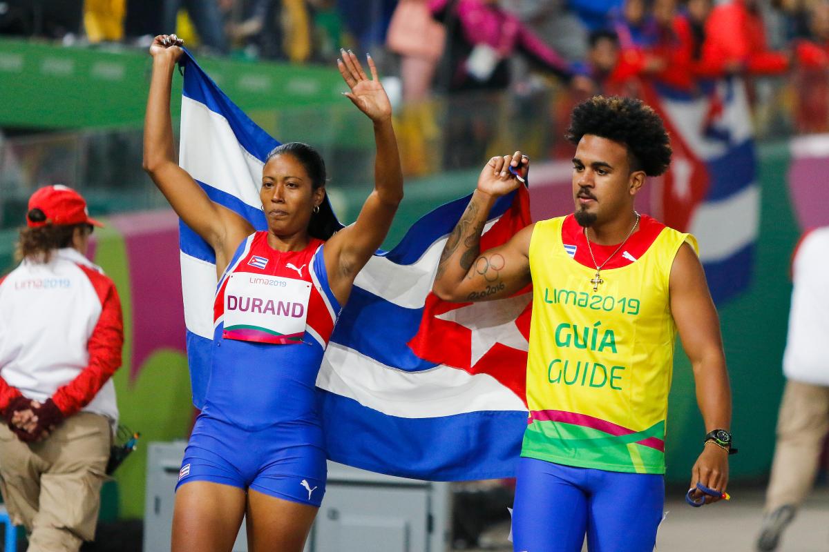 a female vision impaired runner and her male guide hold up the Cuba flag and wave