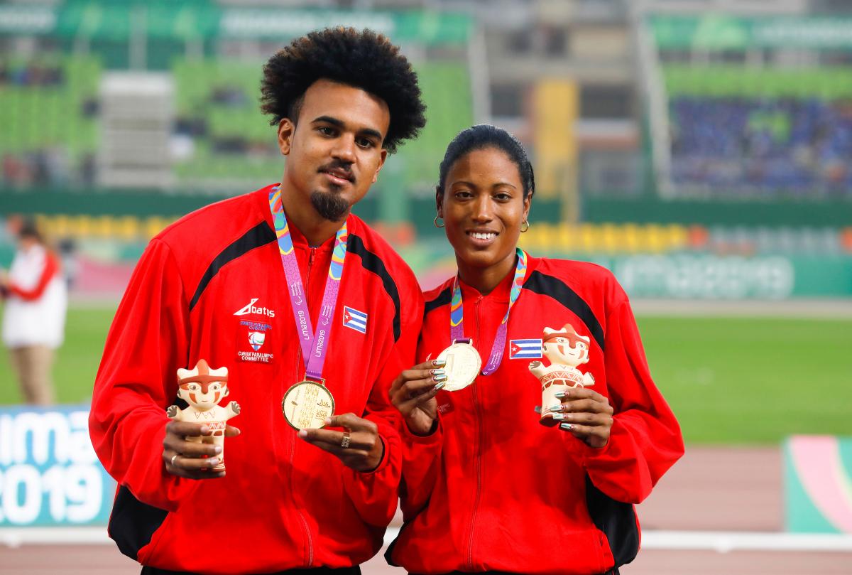 a female vision impaired runner and her guide hold up their gold medals