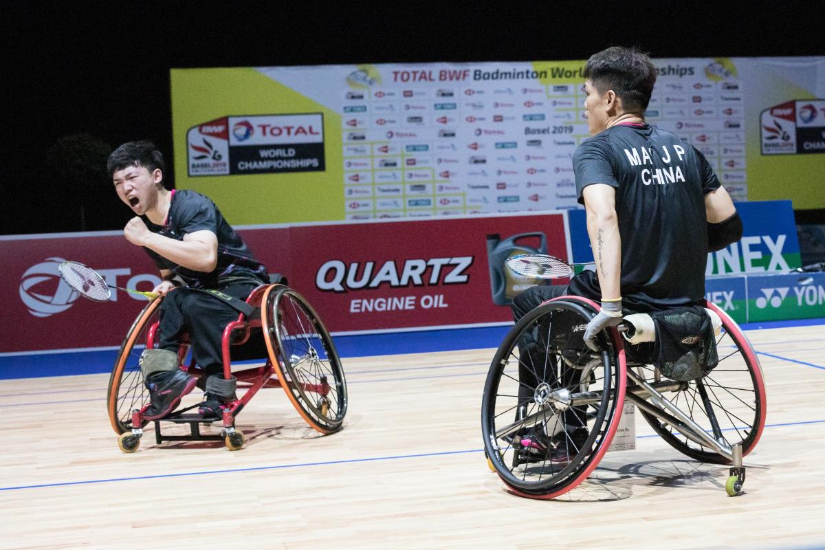 Two male Chinese badminton players in wheelchairs celebrate a point