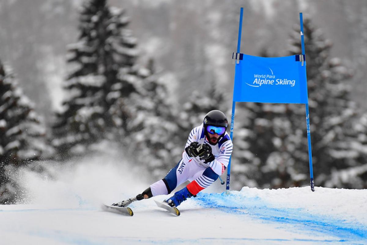 a male Para alpine skier with a prosthetic skiing round a gate