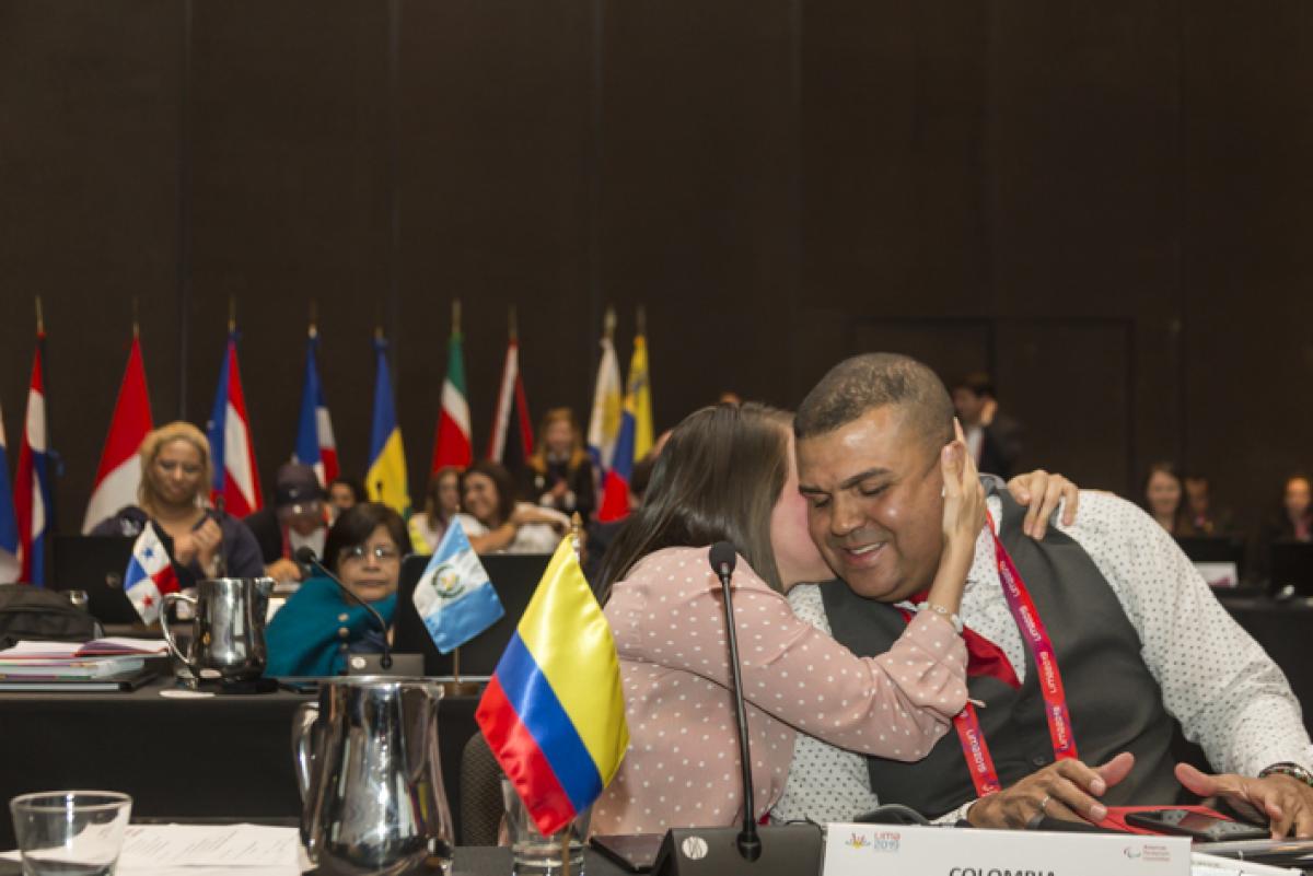 a man sitting at a desk smiling and being hugged by a woman