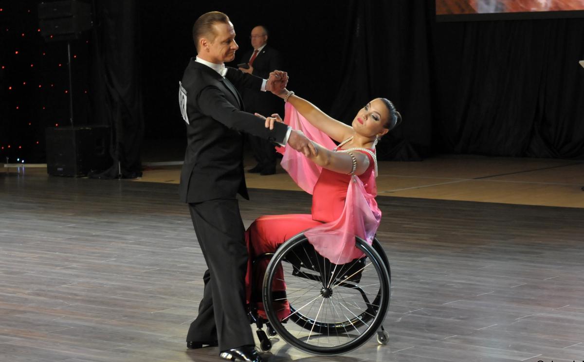 Male standing dancer performs standard dance with female partner in wheelchair