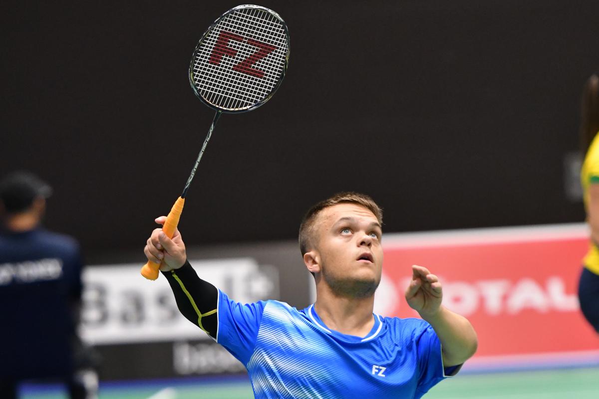 English short statured badminton player looks up about to hit the birdie