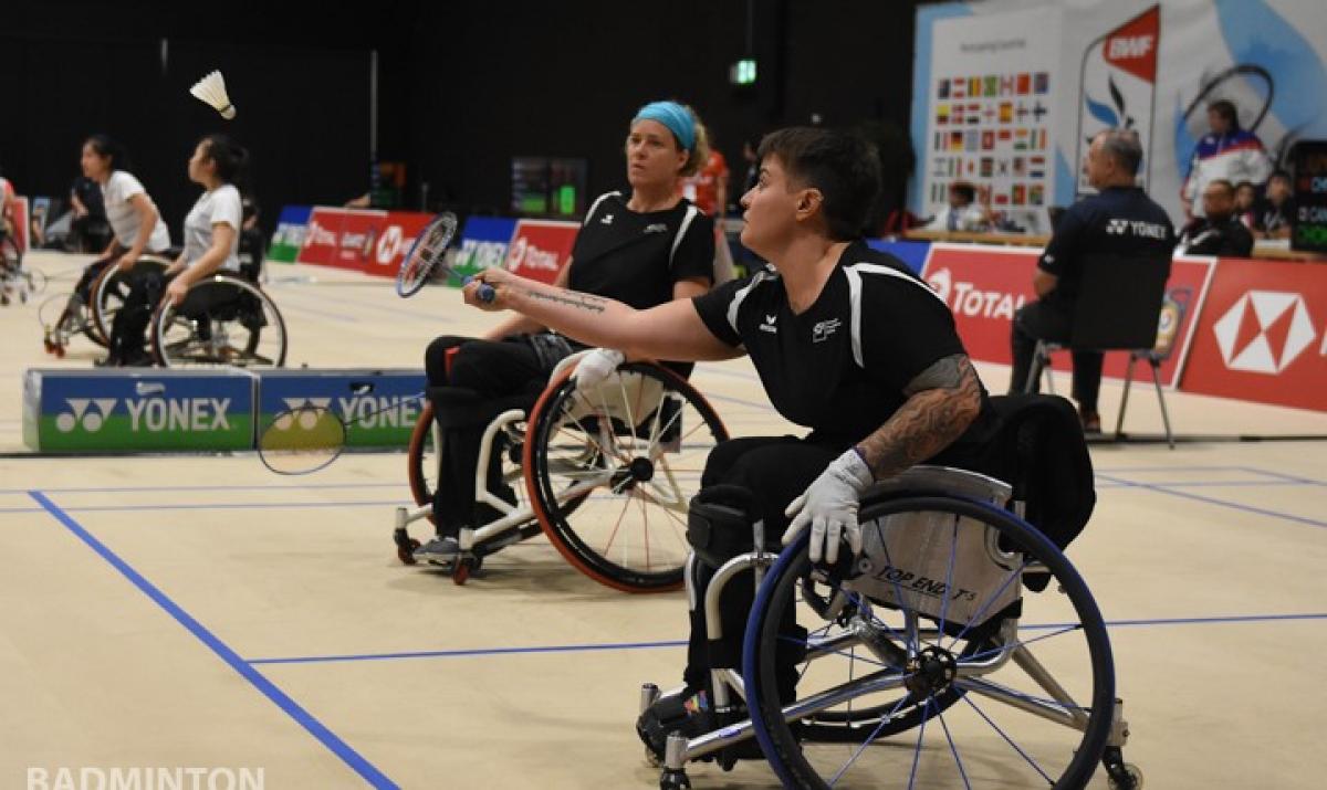 Two females in wheelchairs play badminton 