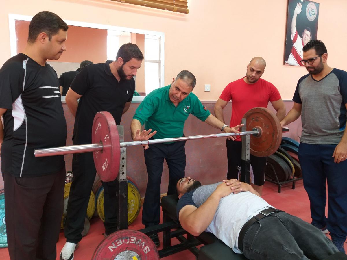 a group of officials standing round an athlete lying on a powerlifting bench