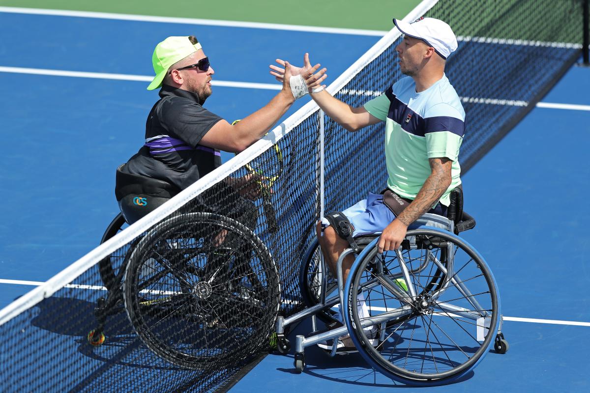 two male wheelchair tennis players shake hands at the net