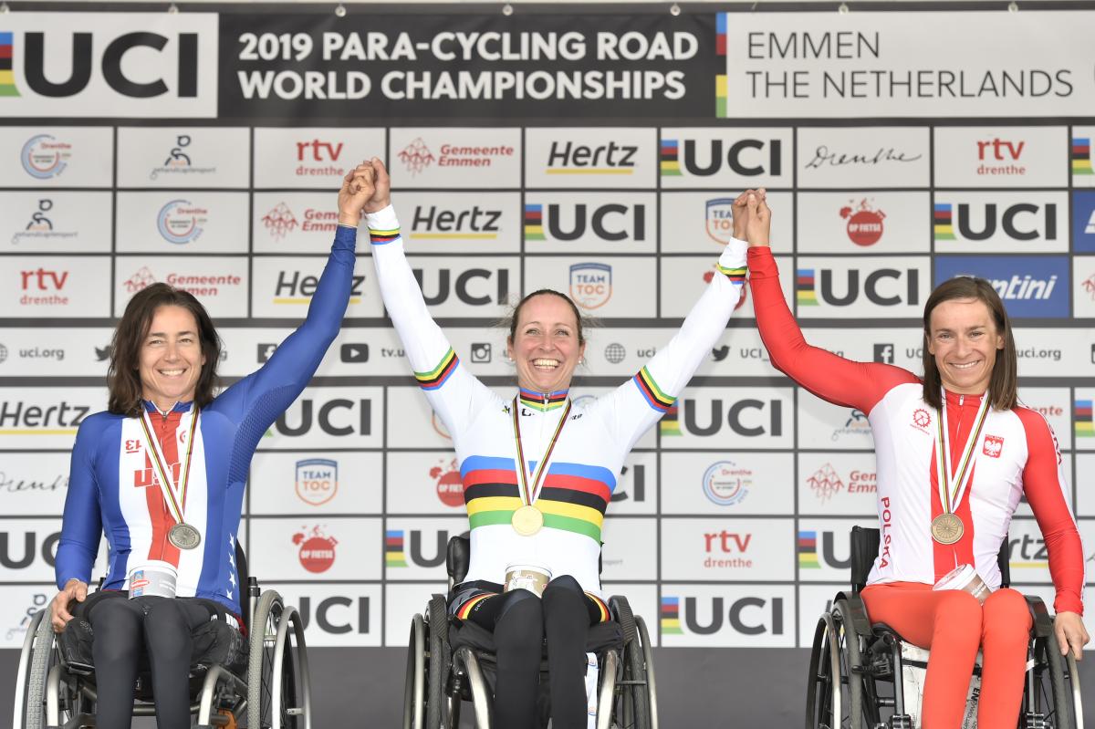 Three wheelchair cyclists hold hands on podium