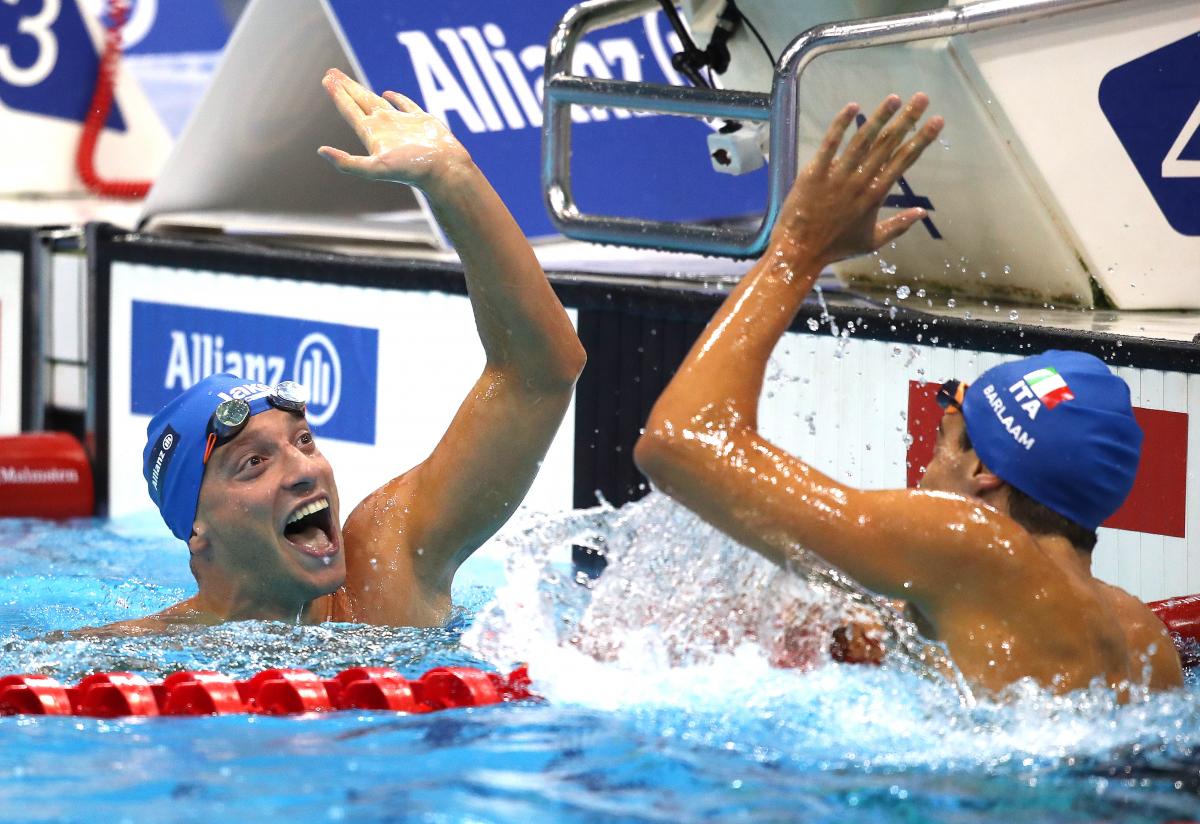 two male Para swimmers high fiving in the water