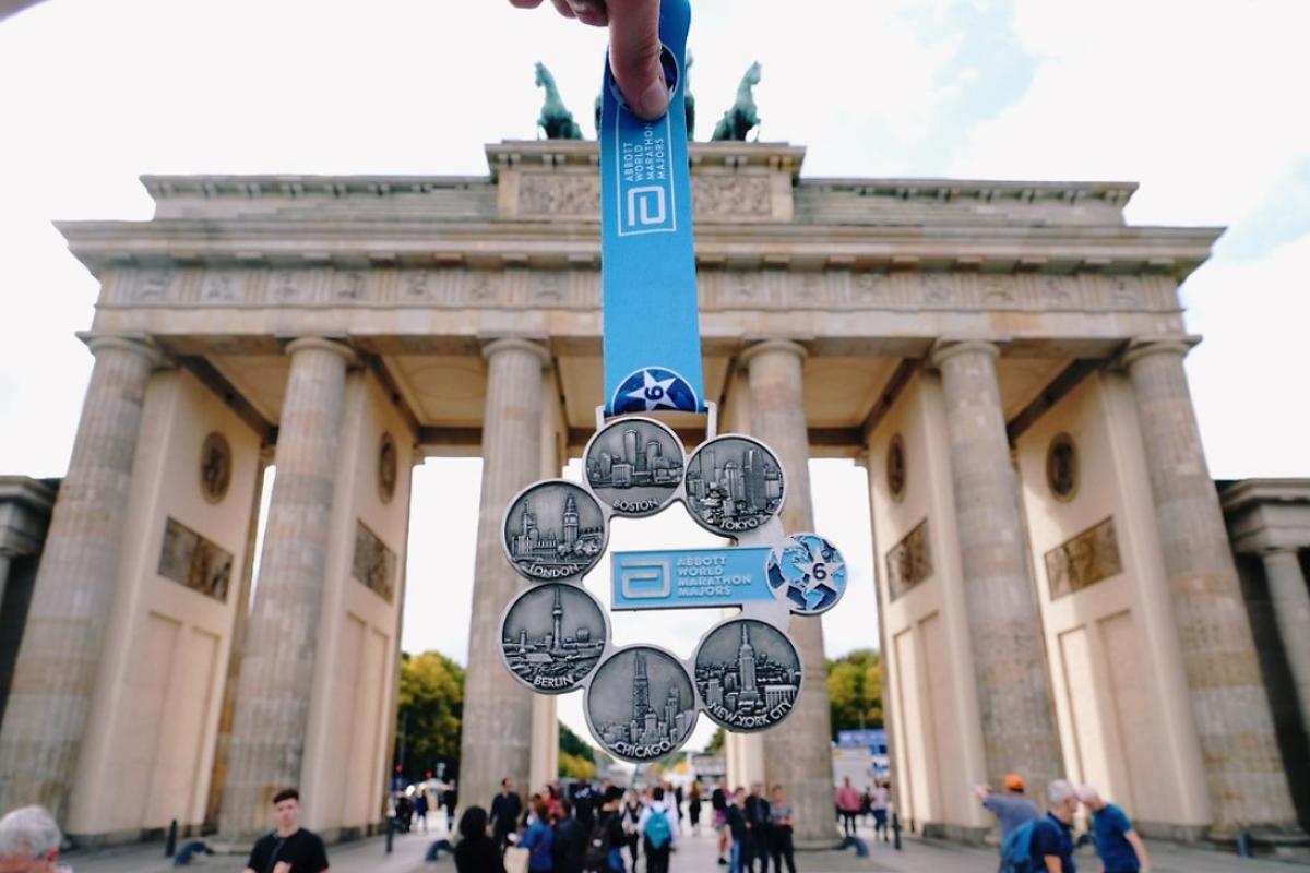 A marathon medal being shown in front of the Brandenburg Gate in Berlin