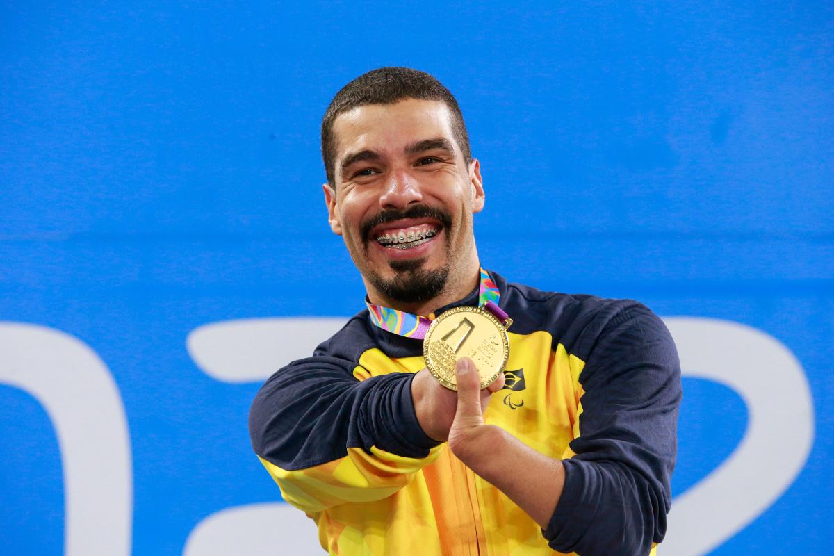 a male Para swimmer holds up his gold medal