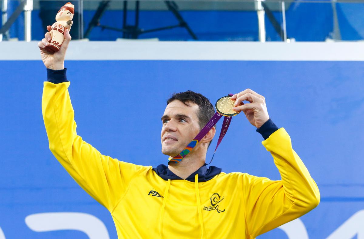 a male Para swimmer holds up his gold medal