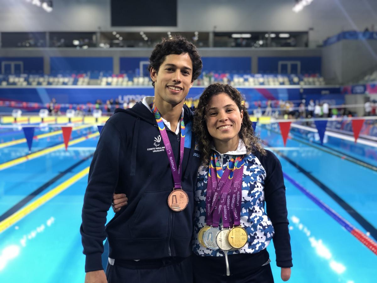 a male and female Para swimmer by the pool with their arms round eachother