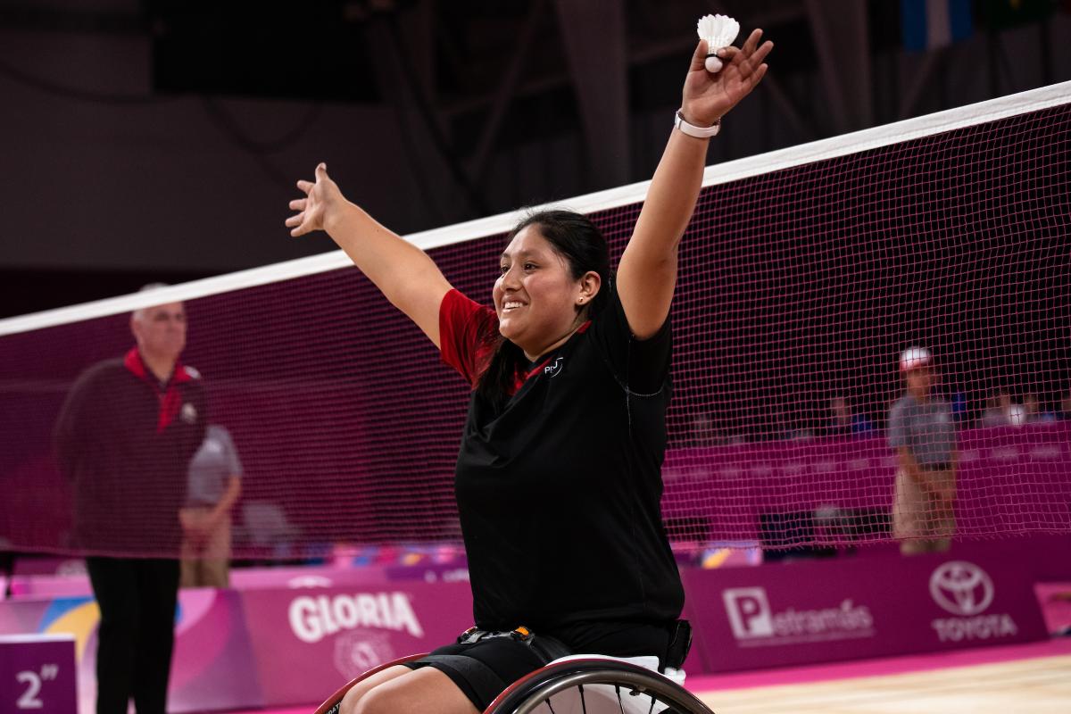 a female wheelchair badminton player throws her arms up in victory