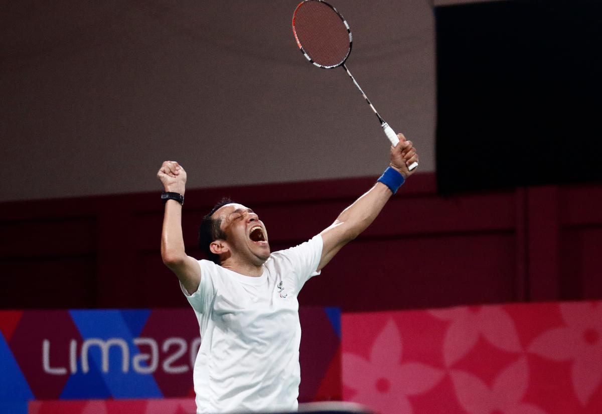 a male Para badminton player raises his fist and racquet into the air in celebration