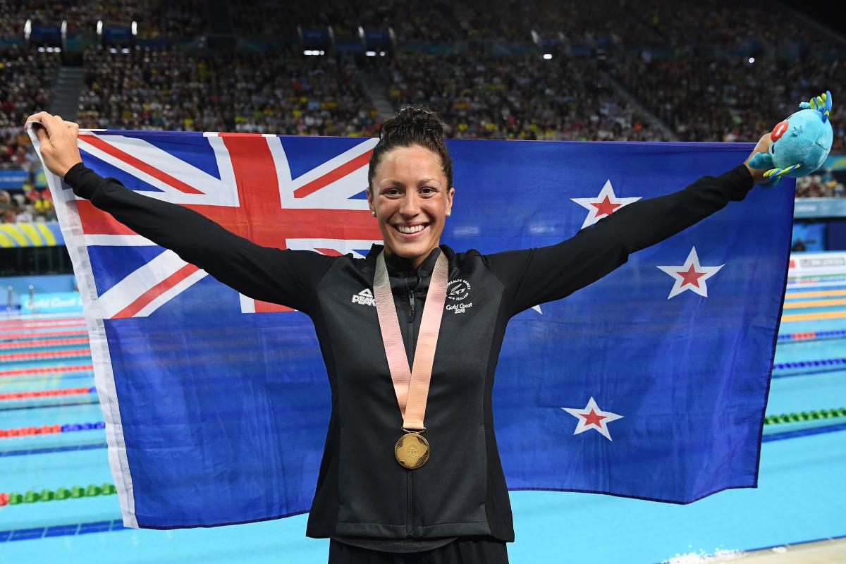 female Para swimmer holding up a New Zealand flag