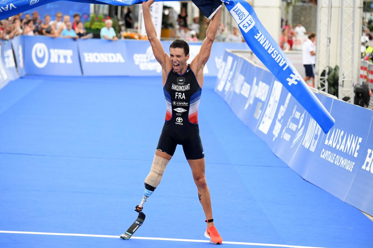 French man with right leg impairment lifts tape over head celebrating a win