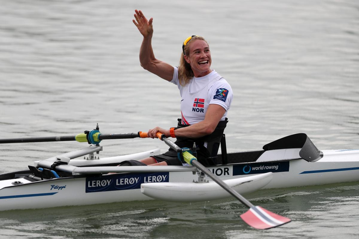 Woman in rowing boat waves at spectators