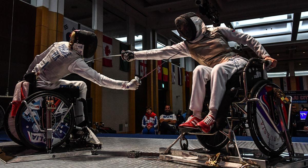 Two wheelchair fencers reach to strike their opponent