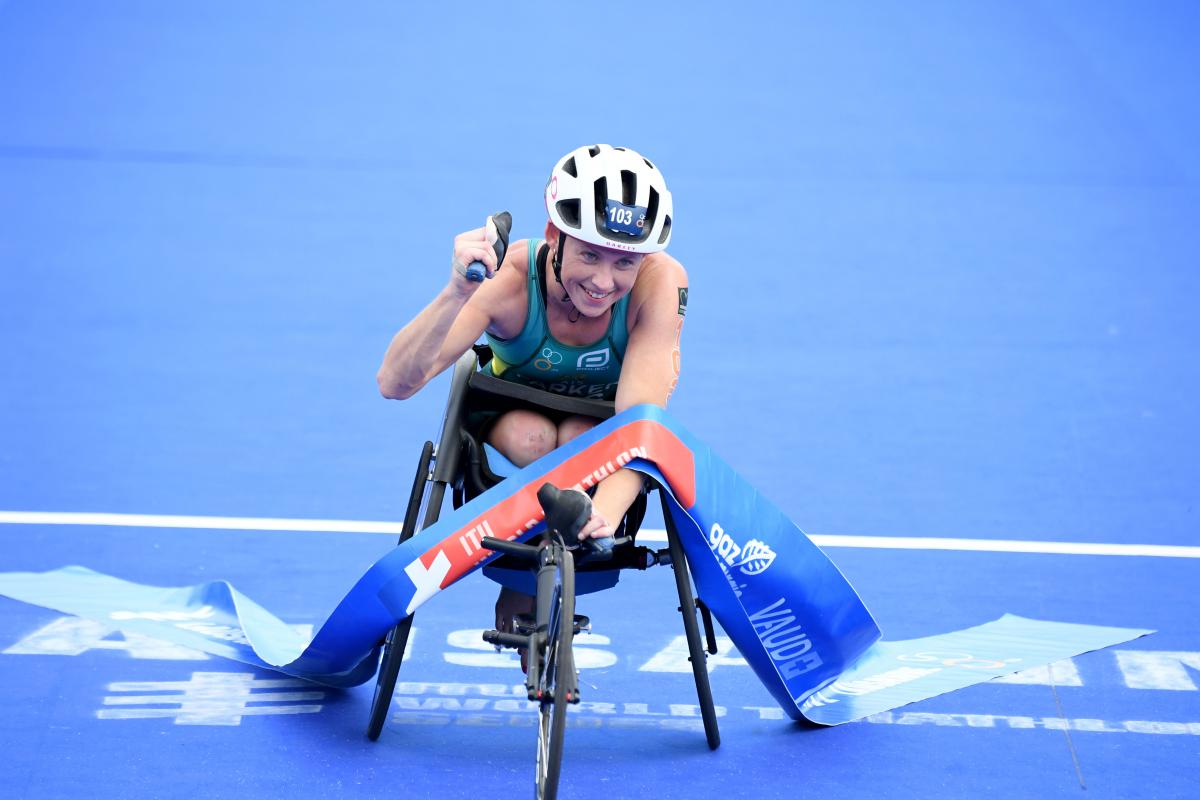 Woman in racing chair crosses finish line tape