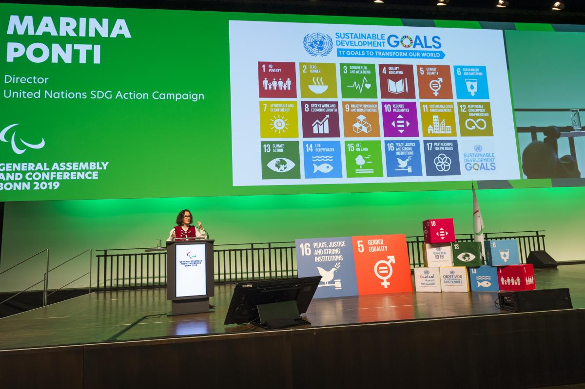 A woman on a stage making a presentation about the UN SDGs