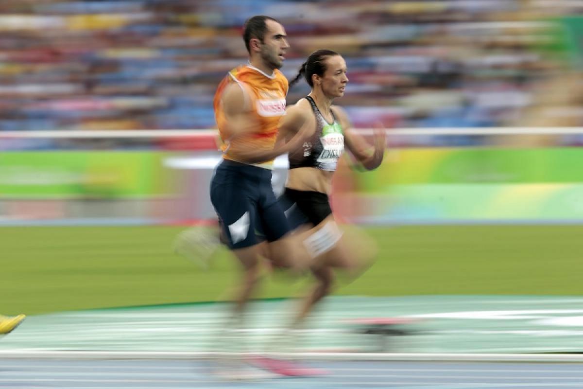 A female sprinter next to her guide on an athletics track