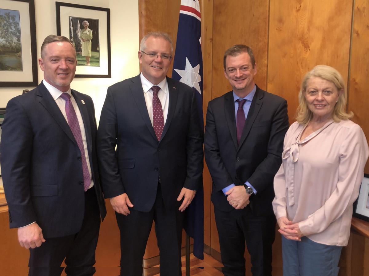 Three men and a woman posing for a picture with a flag of Australia behind them