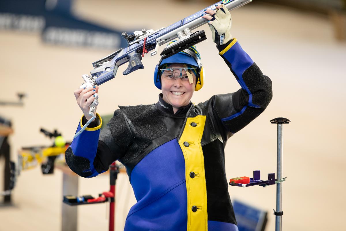 A female shooter smiling a holding her rifle above her head