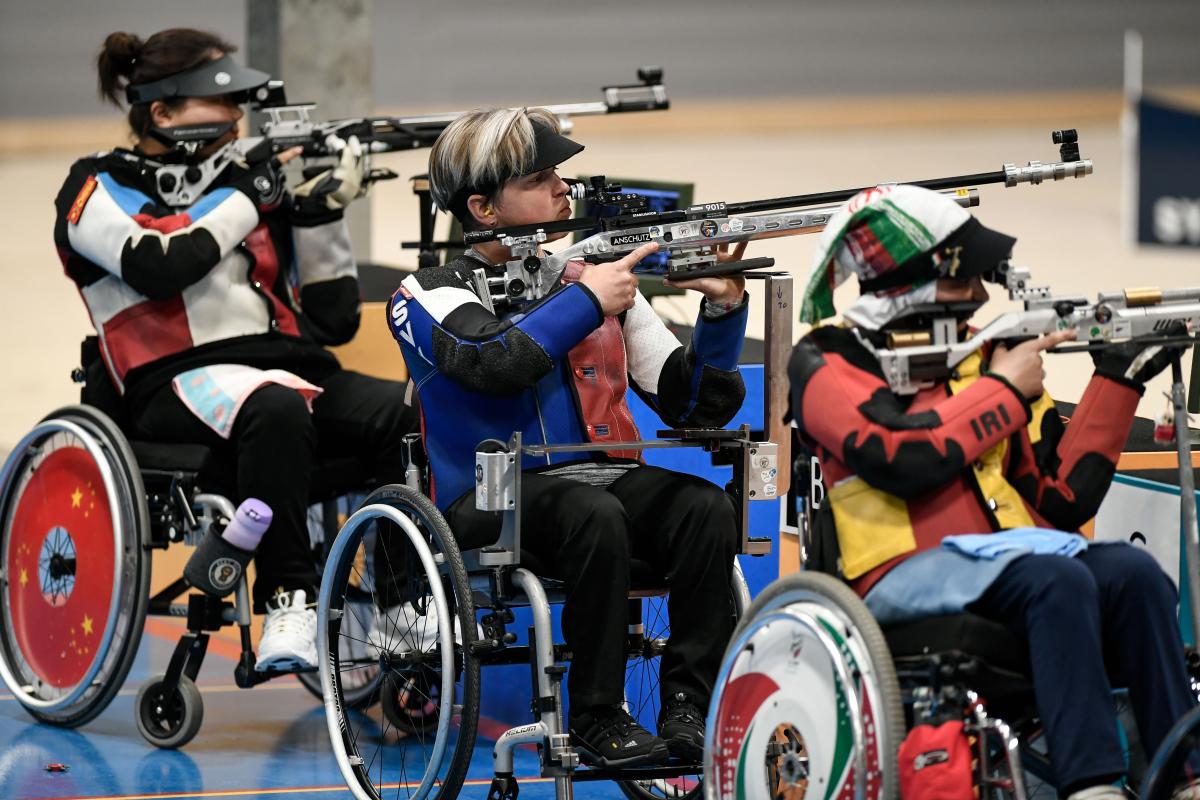 Three female shooters in wheelchairs competing with rifles