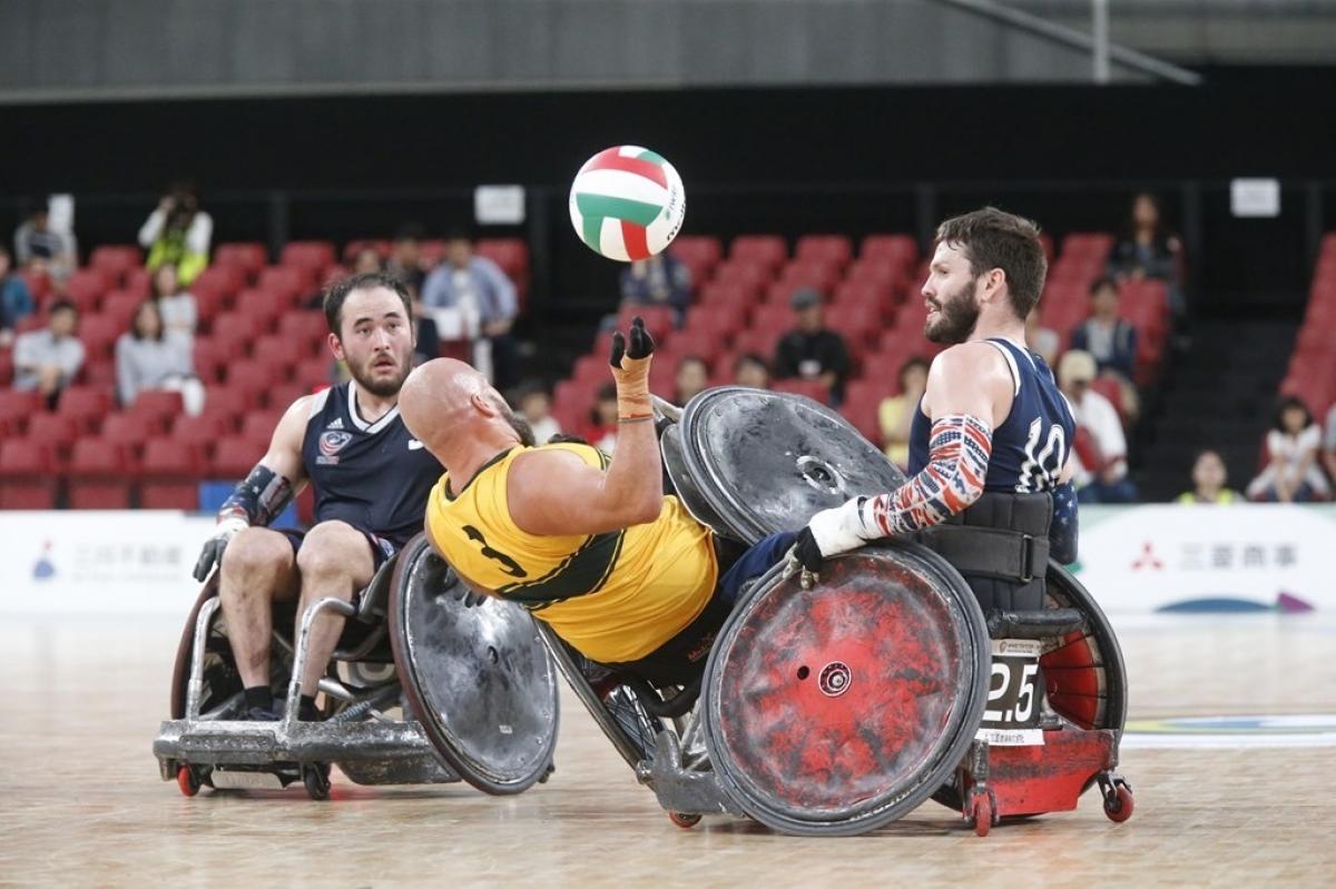 Two wheelchair rugby players knock over an opponent