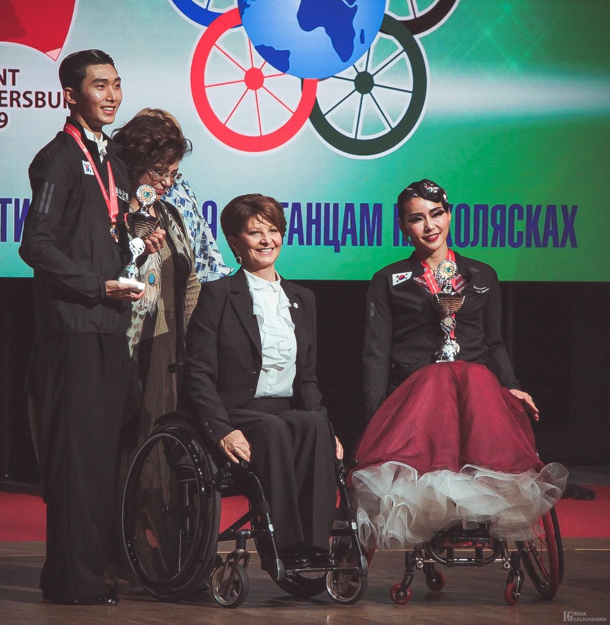 Female dancer in wheelchair and male standing partner on stage with award