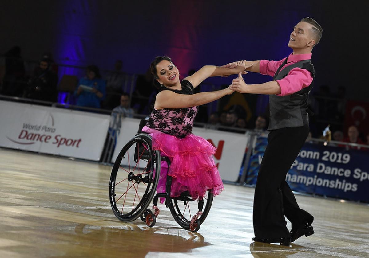 Female dancer in wheelchair and standing male partner dance to quickstep