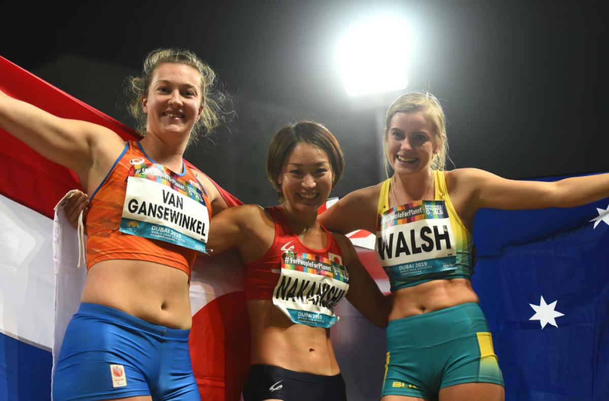 Three female longer jumpers pose for a photo with their respective flags