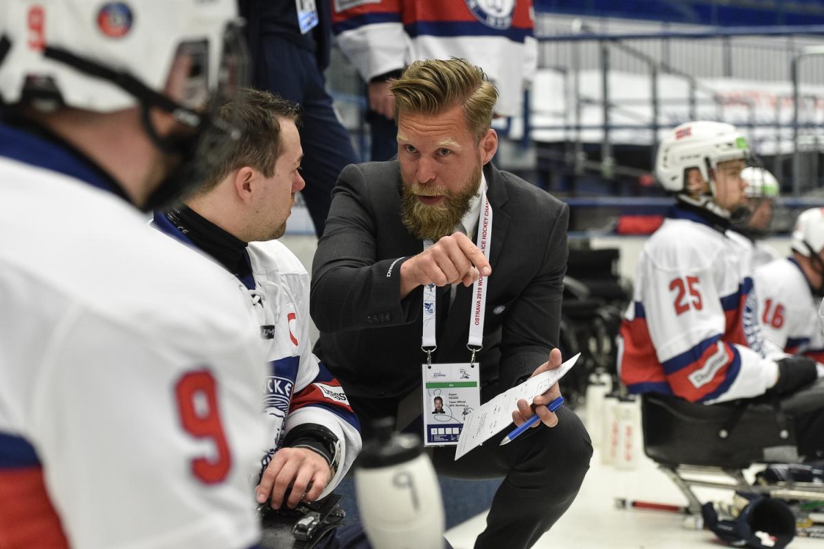 A man in suit talking to a Para ice hockey player on the ice