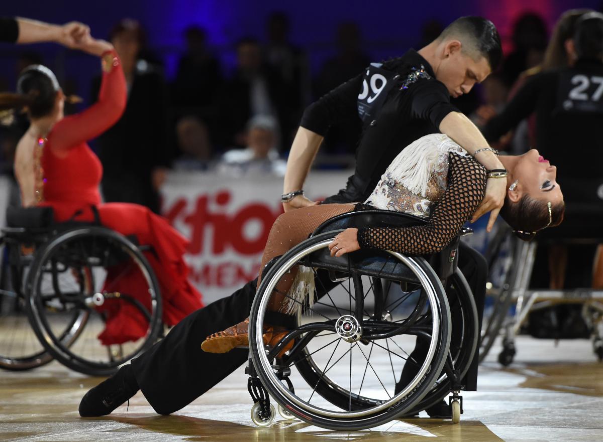Standing male dancer dips his female wheelchair dancer