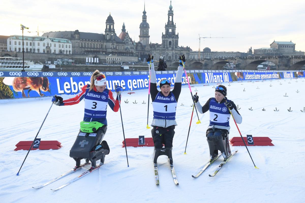 A female sit-skier celebrating between two other skiers