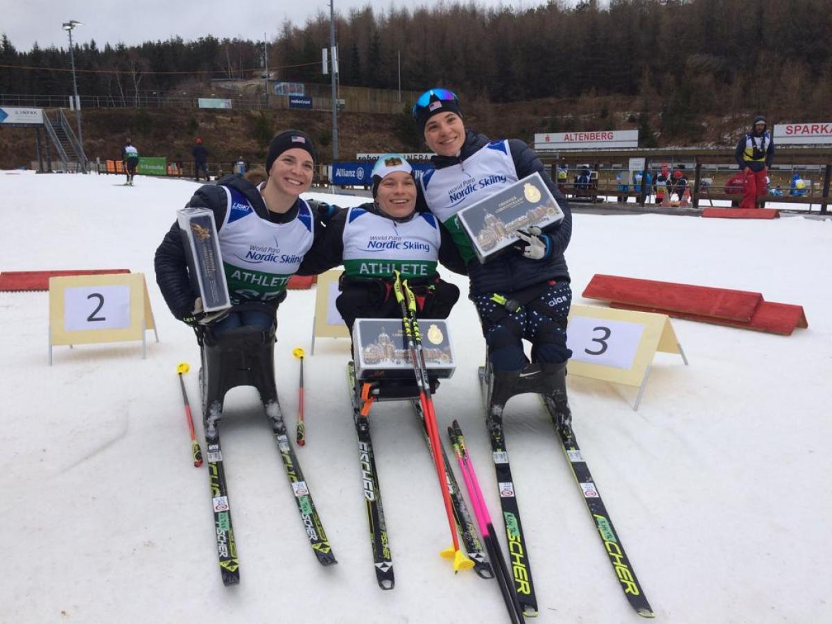 Three female sit-skiers posing with their trophies