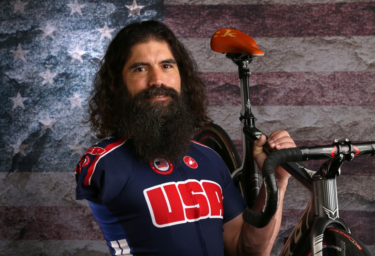 Portrait of man with big beard and missing right arm holdings his bike